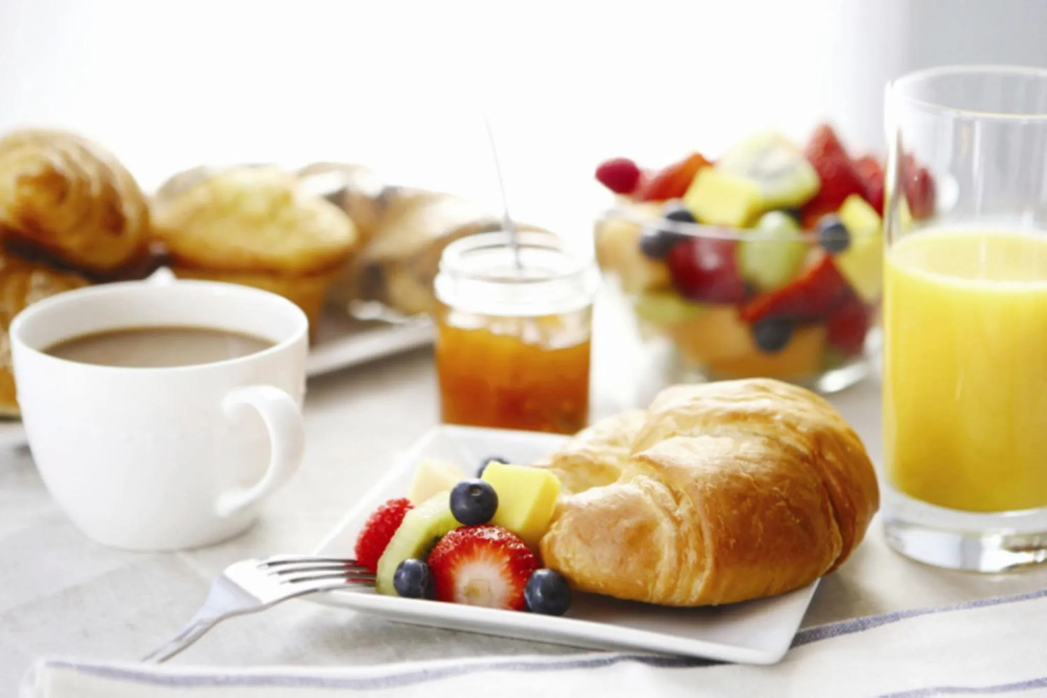 Une table présente un petit-déjeuner avec des viennoiseries, des fruits et une boisson.