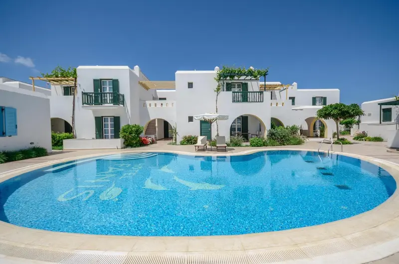 Bâtiment blanc avec des ouvertures bleues surplombant une piscine ensoleillée.