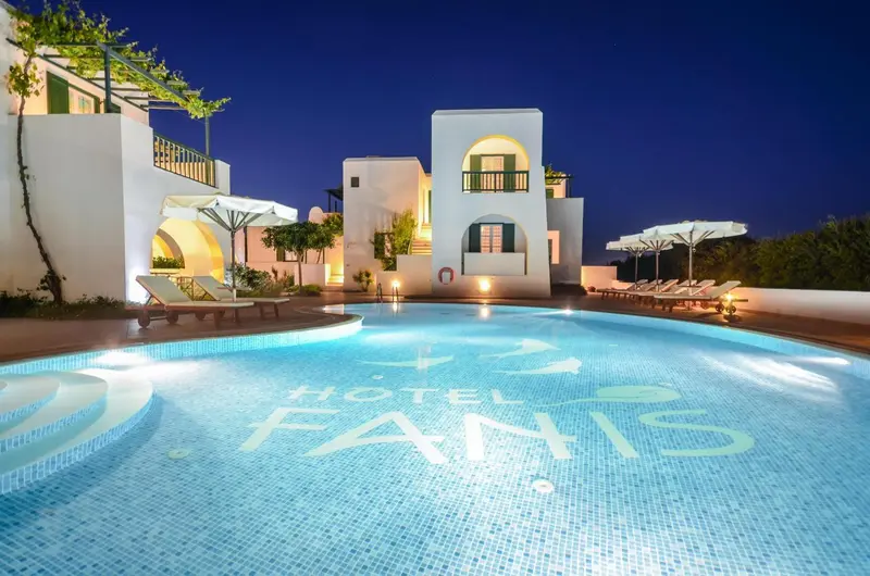 Bâtiment blanc illuminé au bord d'une piscine éclairée la nuit.