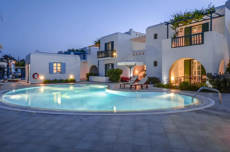 Bâtiment blanc illuminé avec une piscine au premier plan et une végétation soignée.