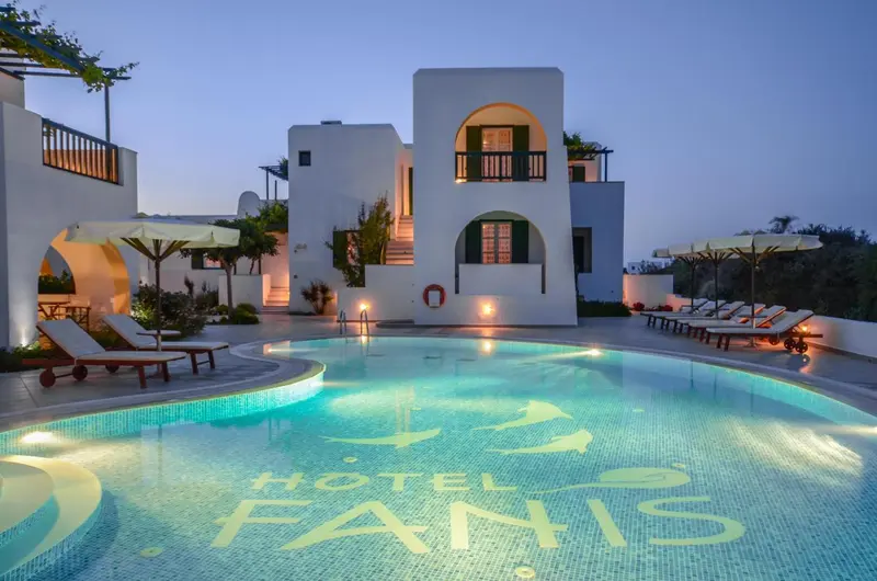 Bâtiment blanc illuminé au bord d'une piscine éclairée la nuit.