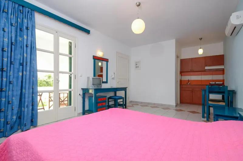 Une chambre lumineuse avec un lit rose et un coin cuisine.