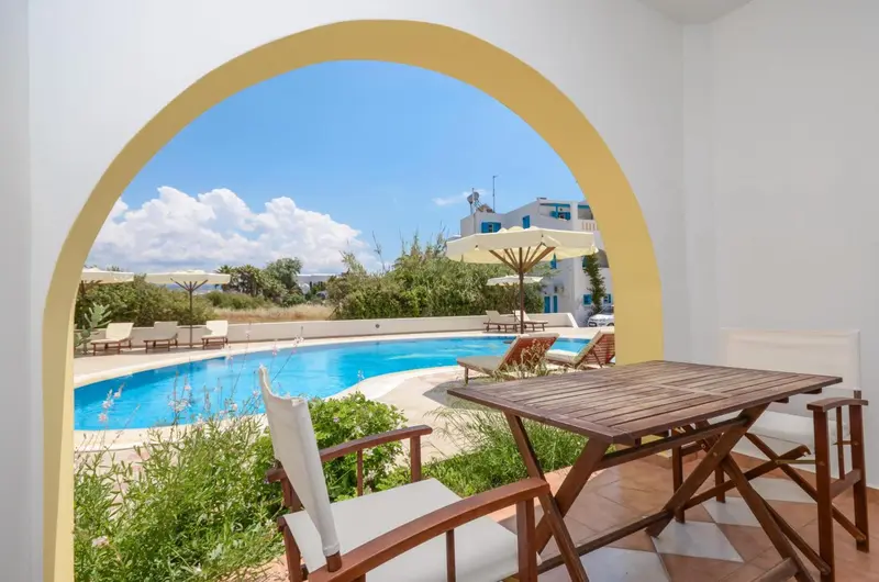 Une table et des chaises en bois sont placées devant une piscine ensoleillée.