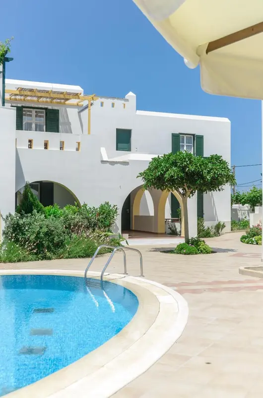 Bâtiment blanc avec des volets verts et une piscine au premier plan.