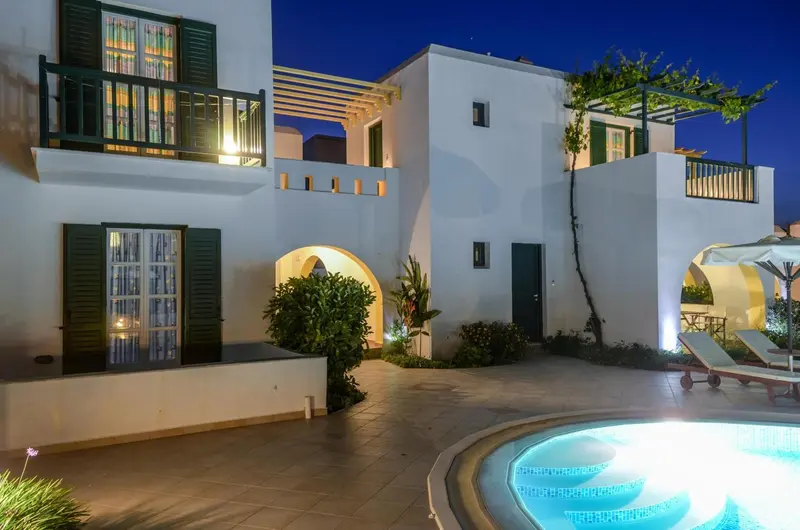 Façade blanche d'un bâtiment avec des balcons et une petite piscine éclairée.
