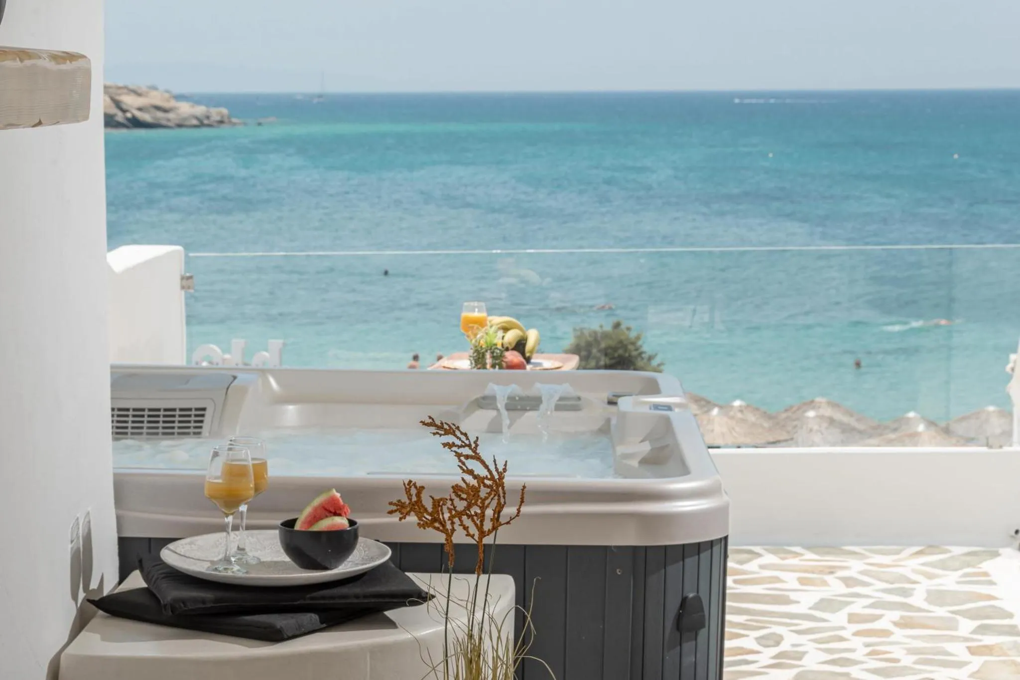 Un jacuzzi avec des boissons et des fruits sur une terrasse offrant une vue sur la mer.