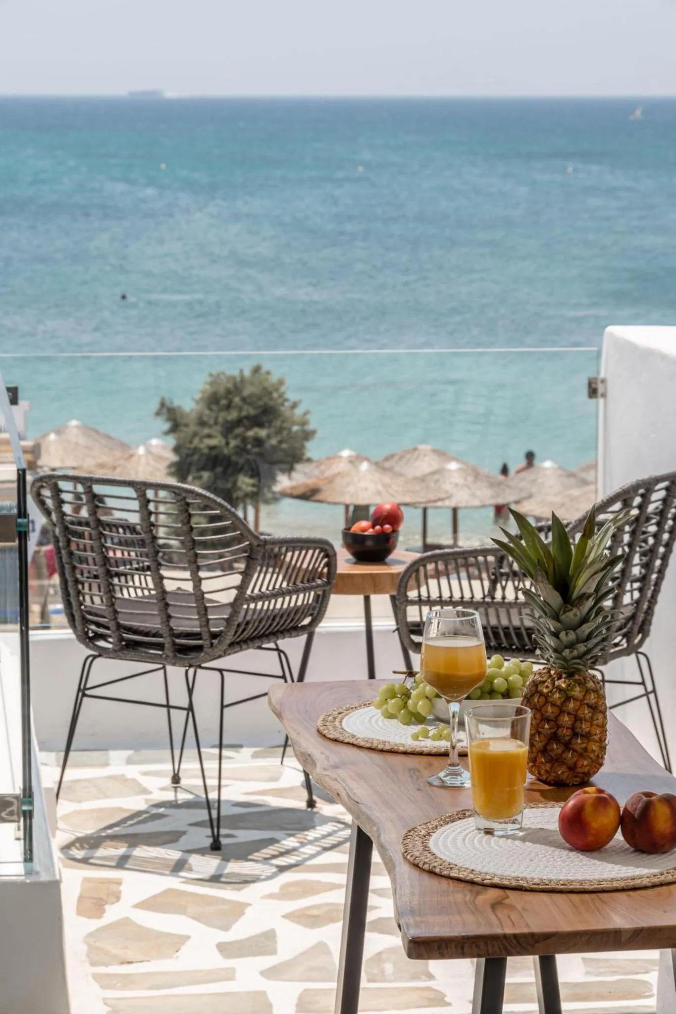Une table basse avec des fruits et des boissons est mise en scène sur une terrasse ensoleillée avec vue sur la mer.