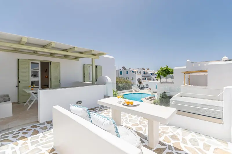 Terrasse aménagée avec salon et table basse donnant sur une piscine et un paysage urbain.