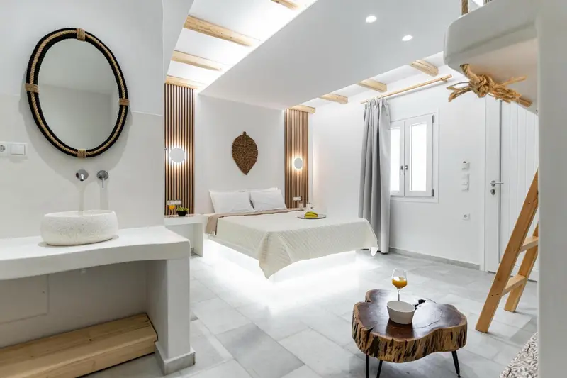 Une chambre lumineuse avec un lit blanc et un miroir rond au-dessus d'un vasque.