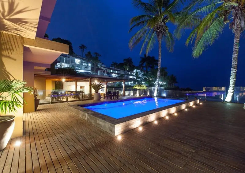 Terrasse lumineuse avec piscine et végétation tropicale au crépuscule.