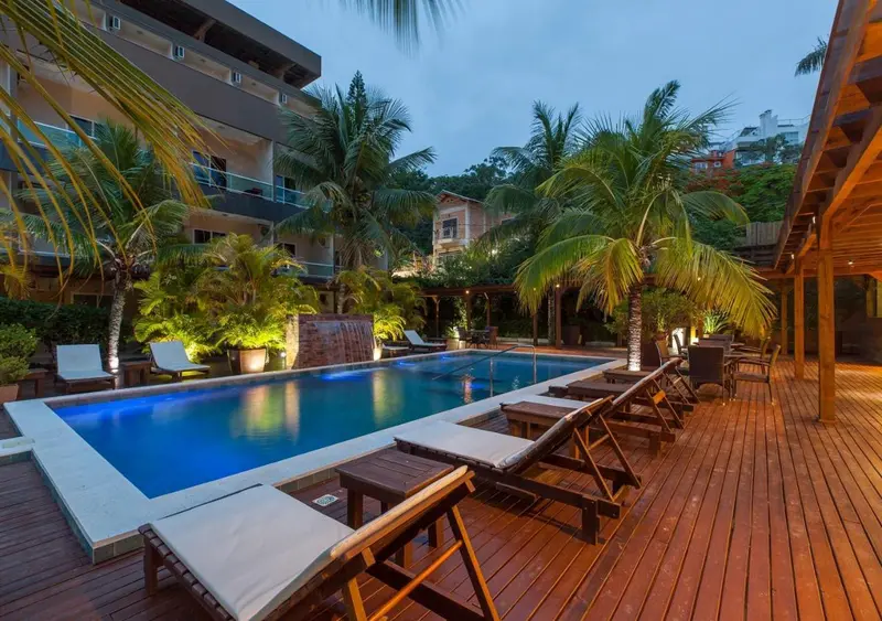 Transats blancs disposés autour d'une piscine illuminée dans un jardin tropical.