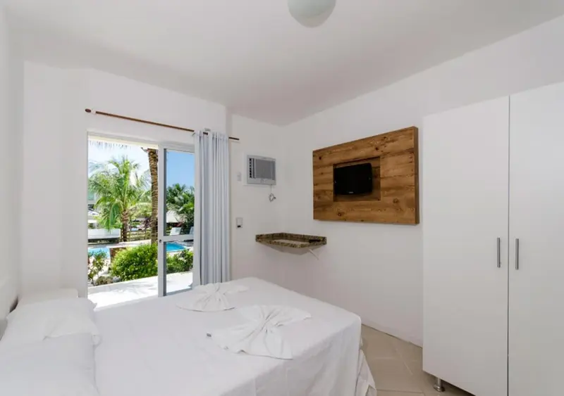 Chambre lumineuse avec un lit blanc et une vue sur une piscine.