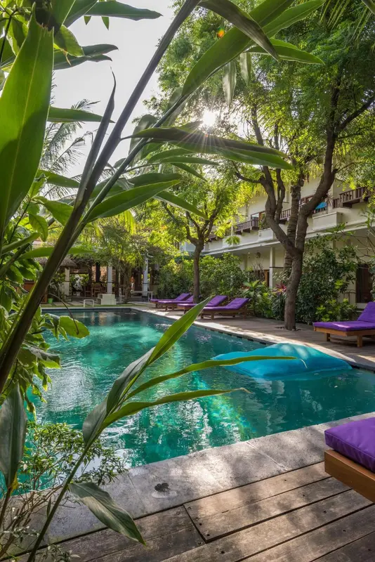 Une piscine turquoise bordée de chaises longues violettes dans un jardin luxuriant.