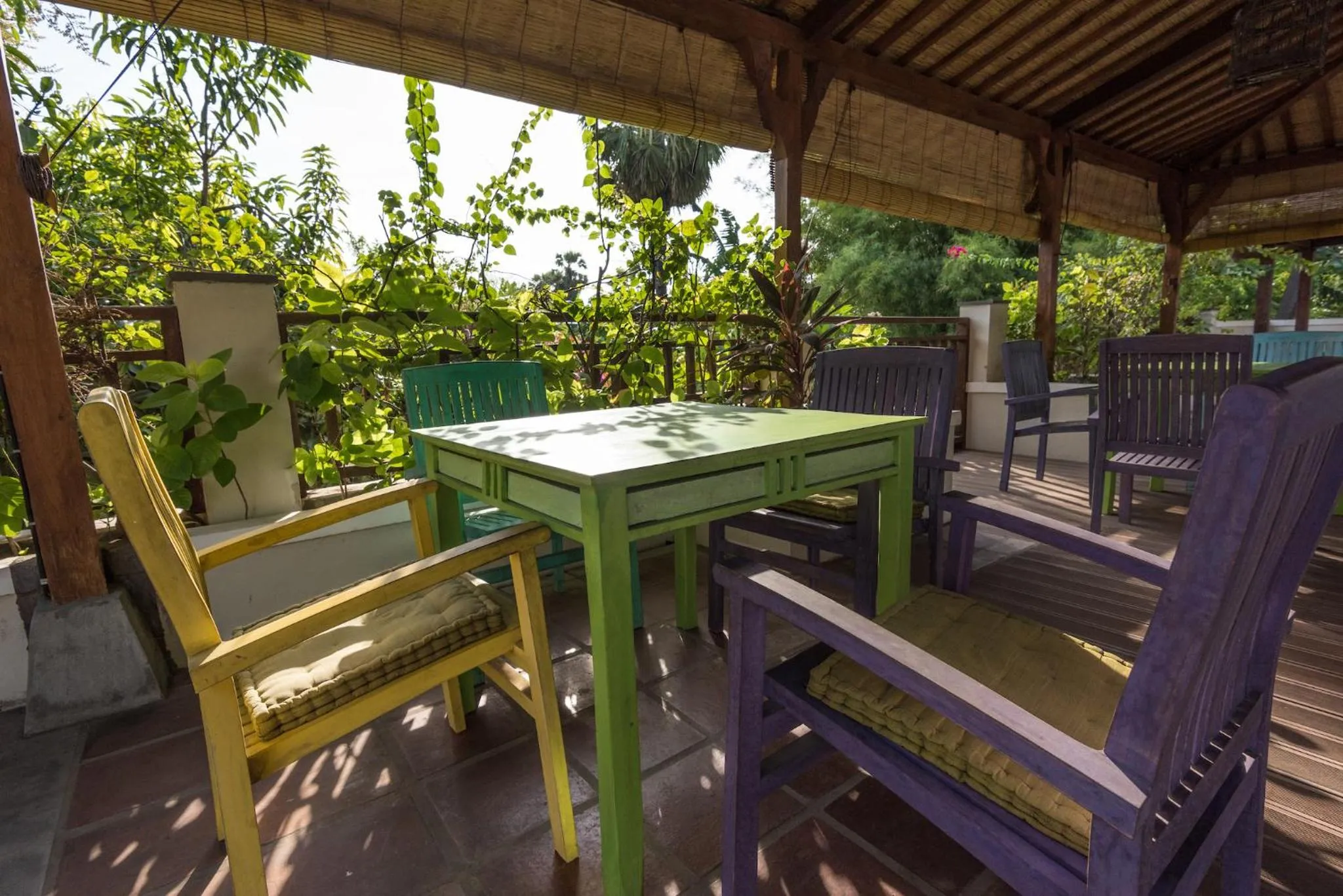Tables et chaises colorées disposées sur une terrasse ombragée.