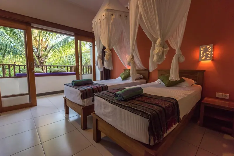 Chambre avec deux lits simples et moustiquaire, donnant sur une végétation luxuriante.