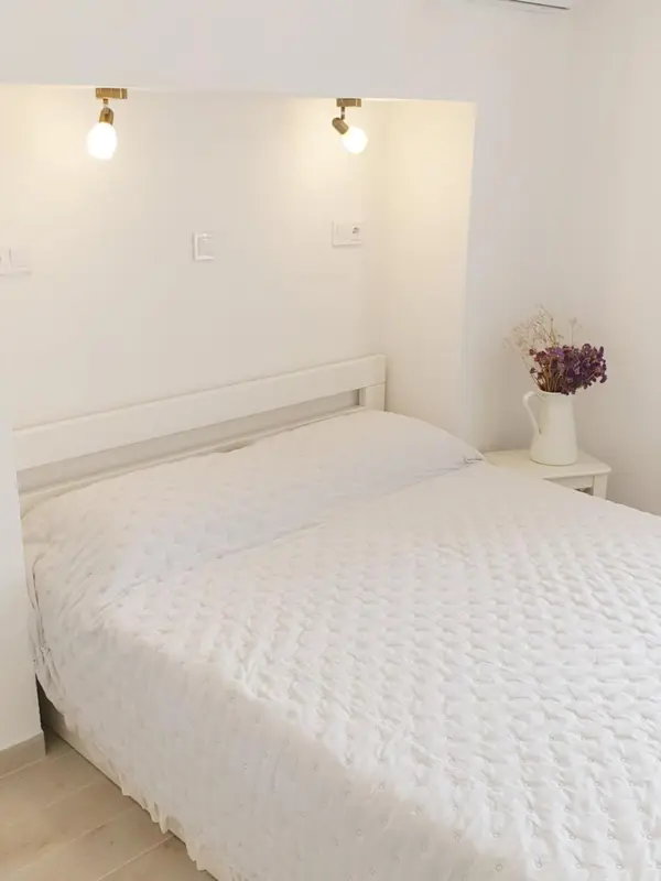 Une chambre lumineuse avec un lit recouvert d'une courtepointe blanche et deux lampes murales.