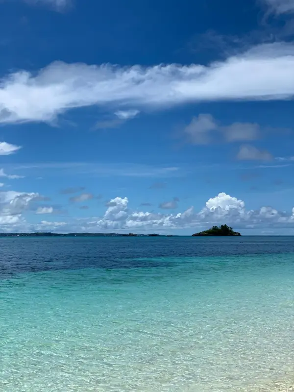 Un ciel bleu nuageux surplombe une eau turquoise et une petite île.