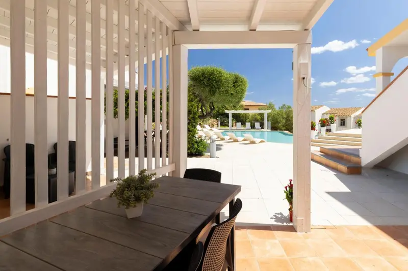 Une table et des chaises se trouvent devant une ouverture sur une piscine ensoleillée.