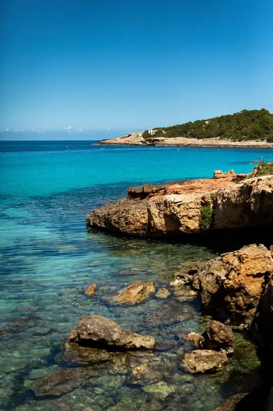 Cote rocheuse surplombant une eau turquoise et une plage de sable.