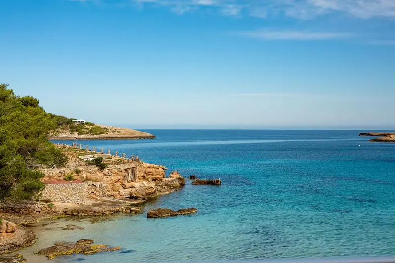 Cote rocheuse surplombant une mer turquoise et une petite plage.