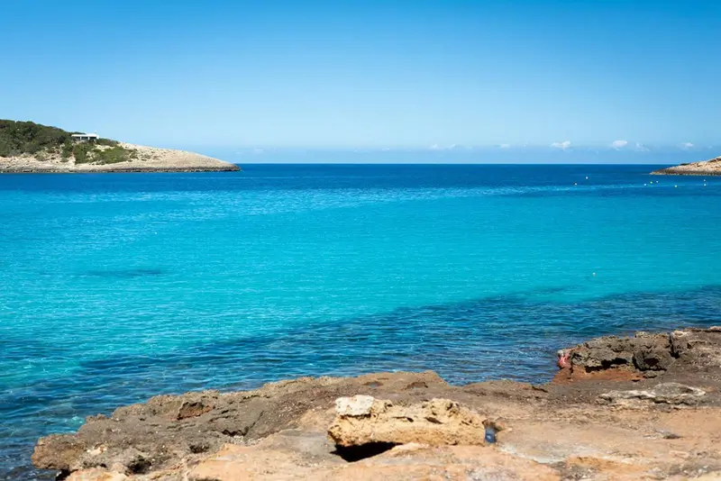 Vue sur une plage de sable fin et une mer turquoise sous un ciel bleu.