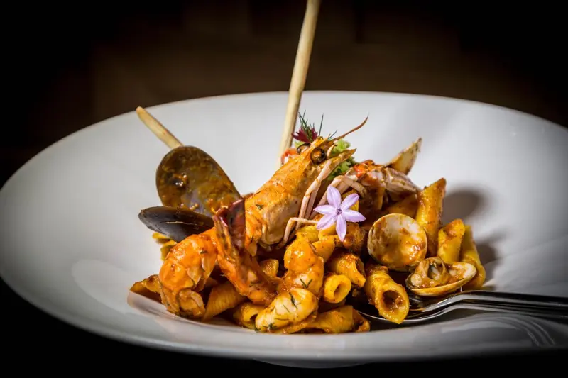 Assiette de pâtes aux fruits de mer et crustacés, décorée de fleurs comestibles.