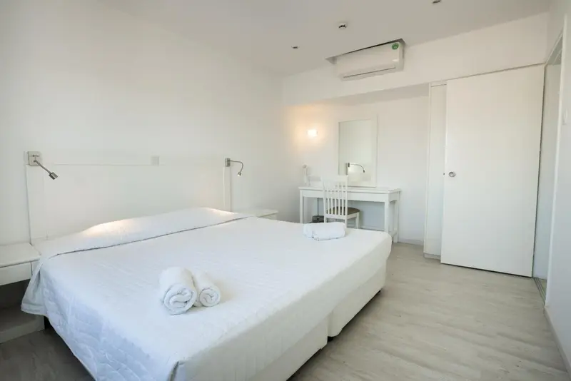 Chambre lumineuse avec un grand lit blanc et un coin bureau.