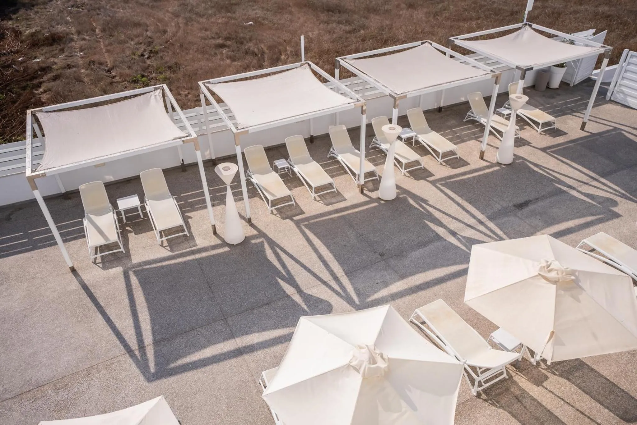 Terrasse avec transats et parasols blancs sous des toiles d'ombrage.