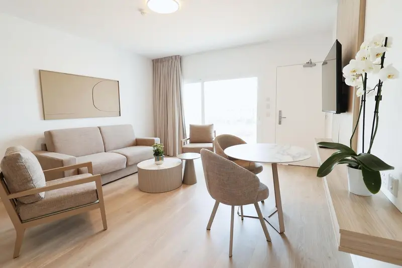 Un salon clair avec canapé, fauteuils et table basse près d'une fenêtre.