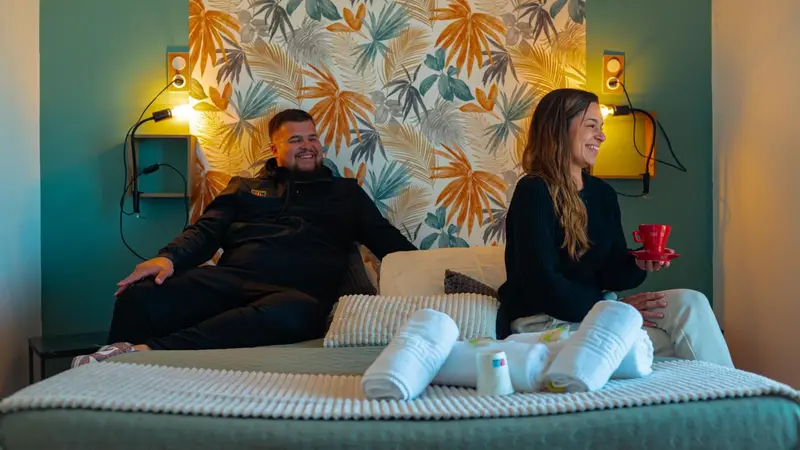 Un couple souriant se détend sur un grand lit dans une chambre décorée.
