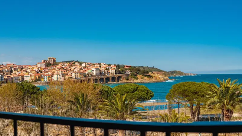 Vue d'une ville côtière avec des bâtiments aux toits rouges et une mer turquoise.