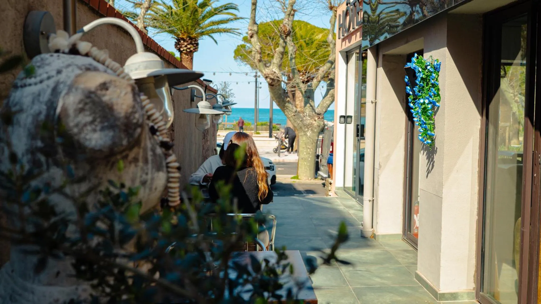 Terrasse ombragée avec tables et végétation en bord de mer.