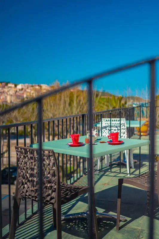 Une table turquoise avec des tasses et une théière sur une terrasse ensoleillée.