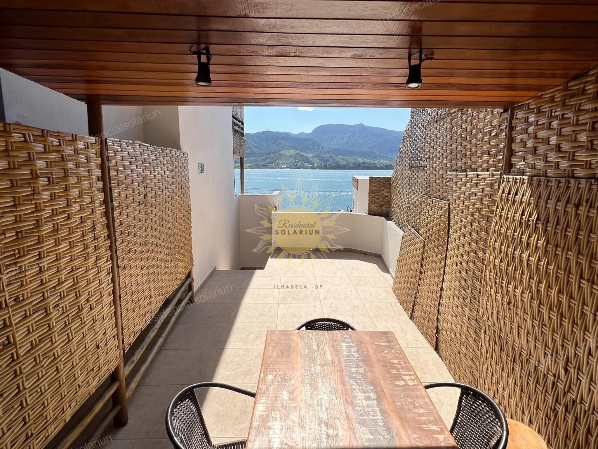 Terrasse ombragée avec mobilier en bois et vue sur la mer.