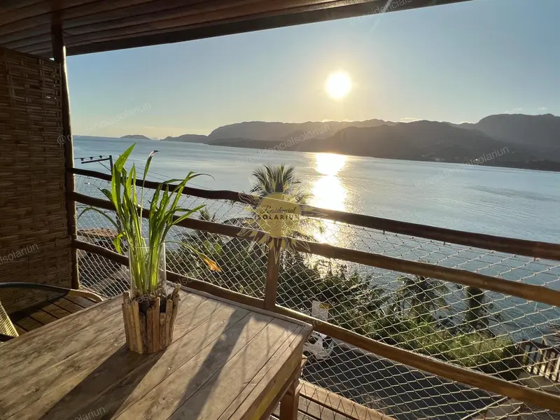 Une terrasse en bois offre une vue sur la mer et les montagnes au coucher du soleil.