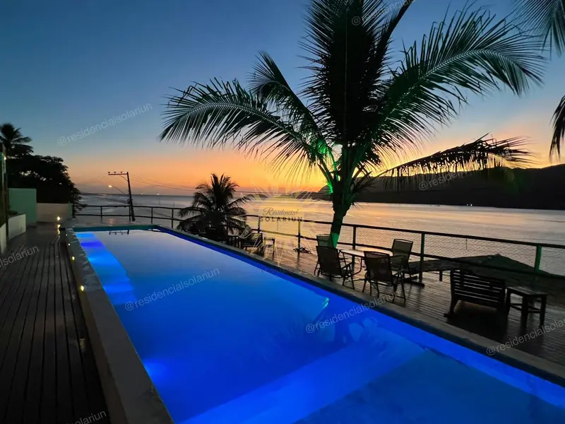 Piscine illuminée avec transats et palmiers au coucher du soleil.