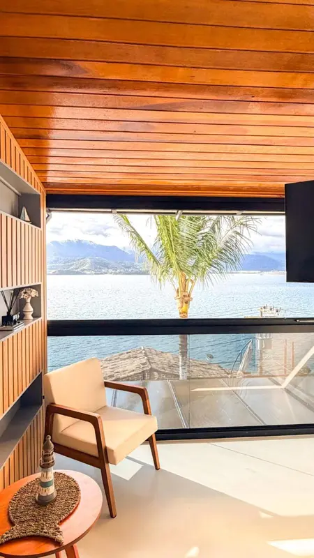 Un fauteuil en bois clair se trouve dans un espace intérieur lumineux avec vue sur la mer.