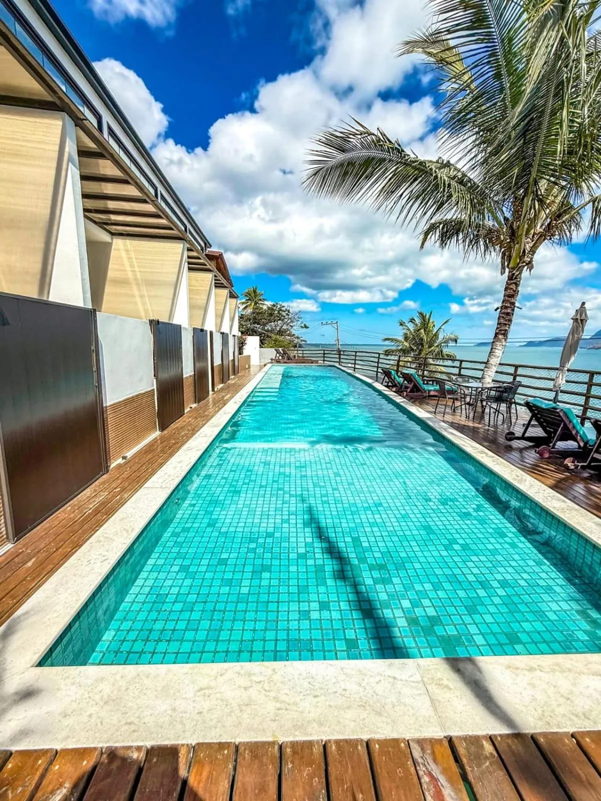 Une piscine rectangulaire bordée d'une terrasse en bois, avec des transats et une vue sur la mer.