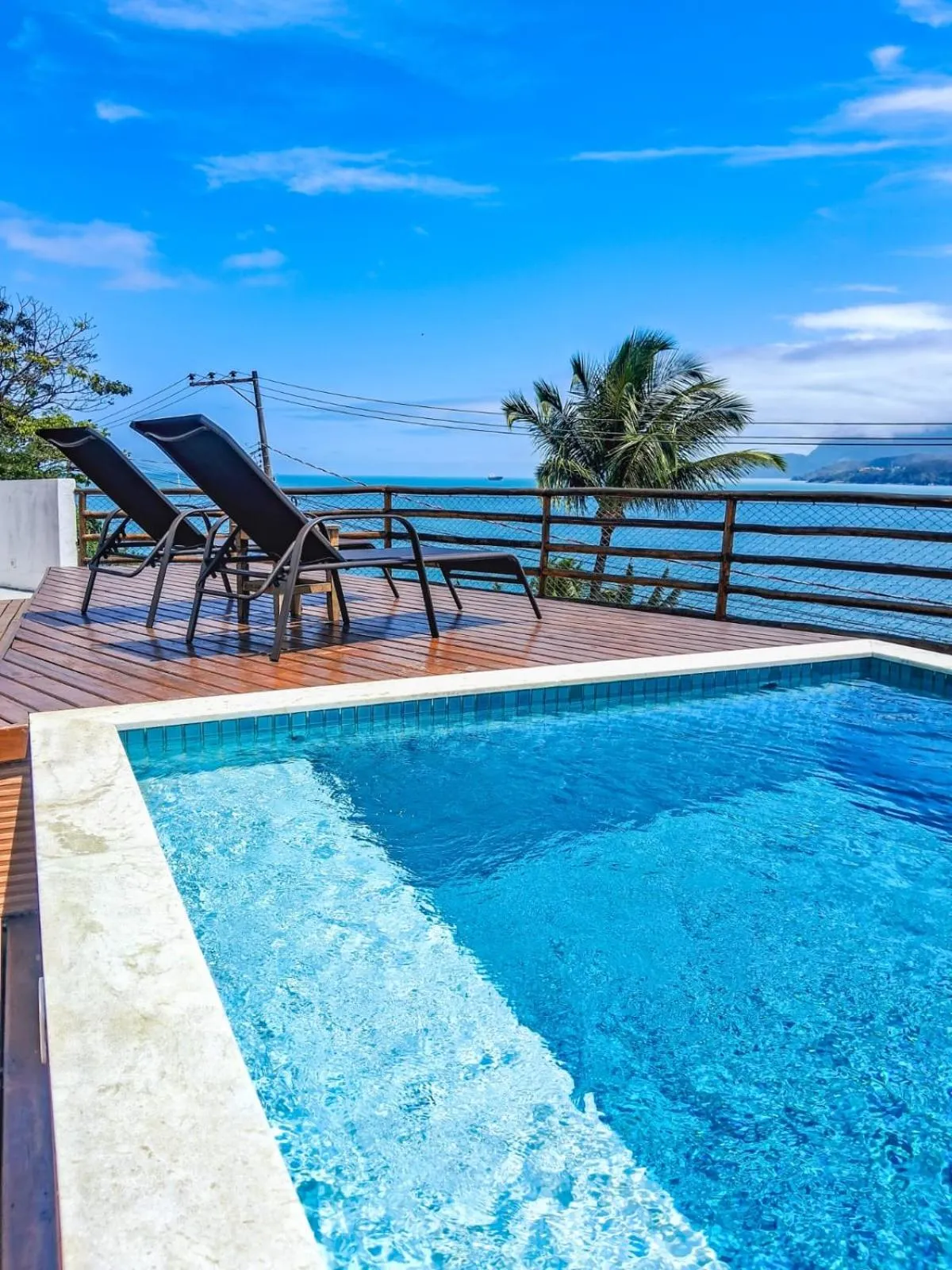 Transats et piscine avec vue sur la mer et la végétation.