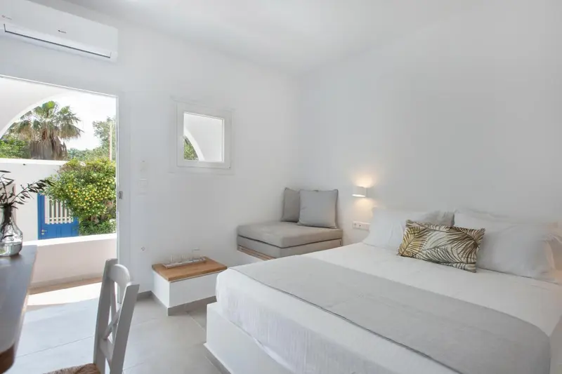 Chambre lumineuse avec un lit et un coin salon donnant sur une vue extérieure.