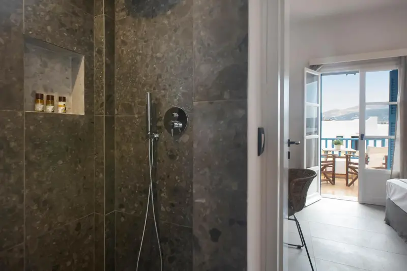 Douche à l'italienne dans une salle de bain carrelée, avec une vue sur une terrasse et la mer au loin.