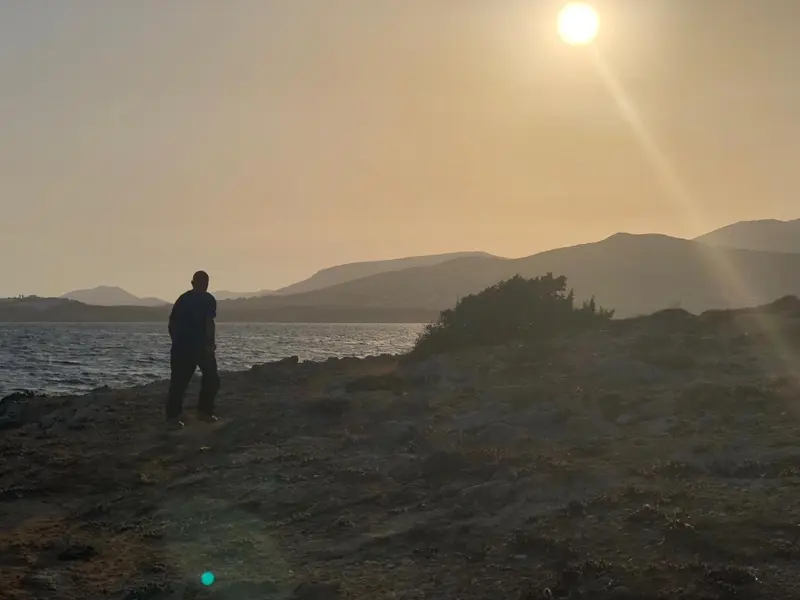 Une personne se tient face à la mer au coucher du soleil.