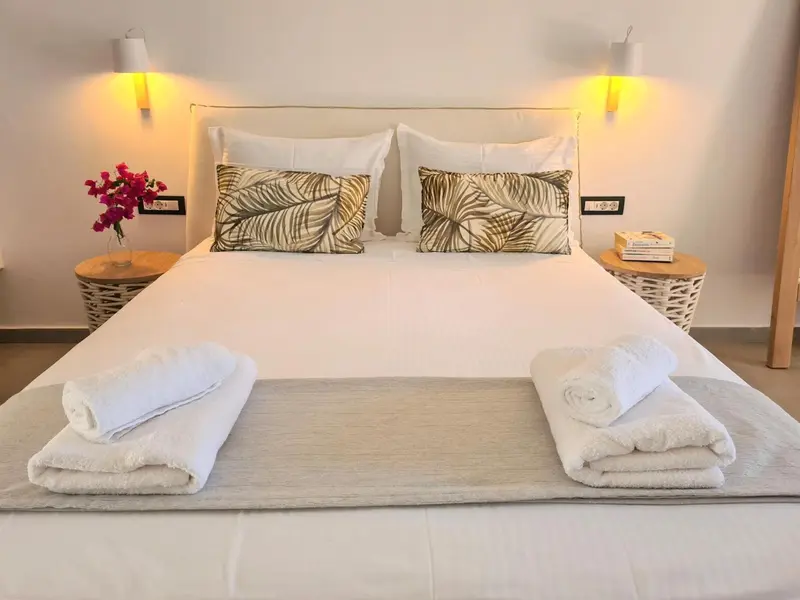 Une chambre lumineuse avec un grand lit recouvert de linge blanc et décoré de coussins.