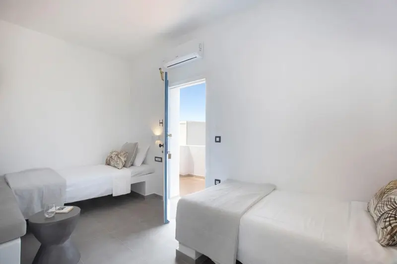 Chambre lumineuse avec deux lits simples et une climatisation murale.