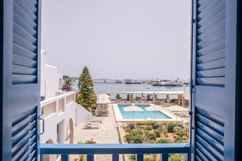 Vue sur une piscine et la mer depuis une fenêtre bleue.