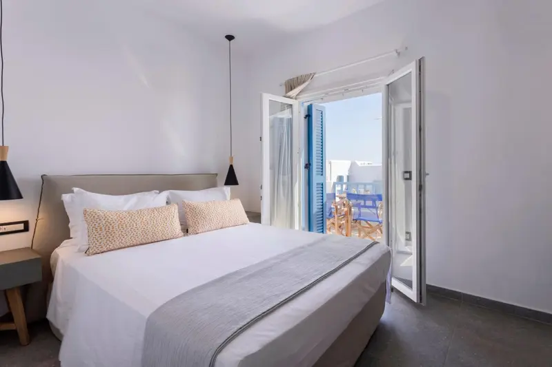 Une chambre lumineuse avec un lit fait et une porte ouverte sur un balcon.