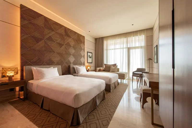 Chambre avec deux lits simples et un espace détente près de la fenêtre.