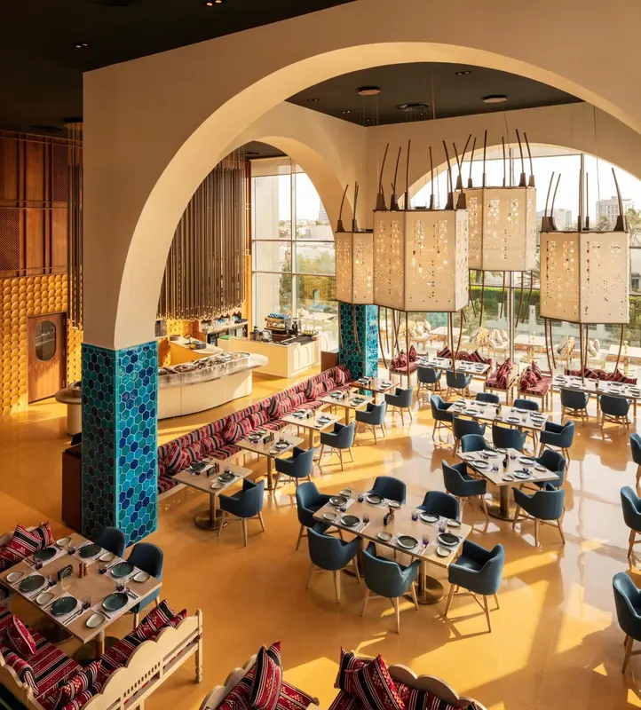 Une salle de restaurant lumineuse avec des tables dressées et des banquettes colorées.