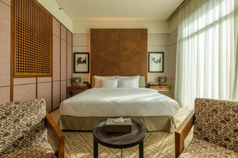 Une chambre lumineuse avec un grand lit et deux fauteuils.