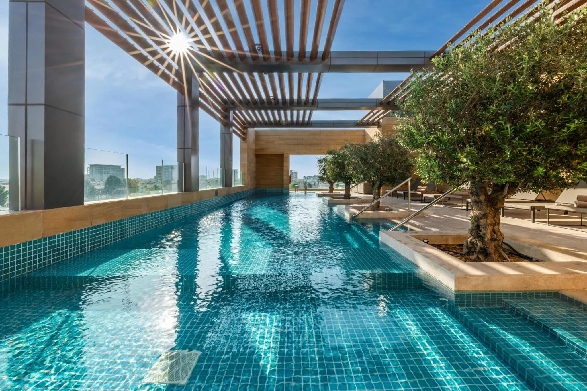 Une piscine rectangulaire extérieure avec des transats et des arbres à proximité.